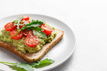 Avocado rye bread toast with cherry tomatoes and arugula on bright background, healthy vegan sandwich.