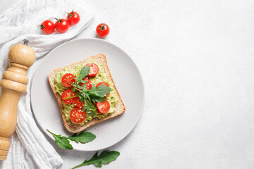 Avocado rye bread toast with cherry tomatoes and arugula on bright background, healthy vegan sandwich.