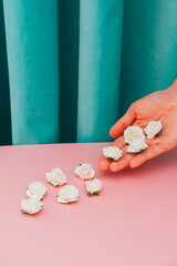 Hand holds white flowers among floral composition. Pink and green curtain background. Retro fashion aesthetic.
