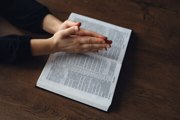 Woman hands on Bible. she is reading and praying over bible in a dark space over wooden table