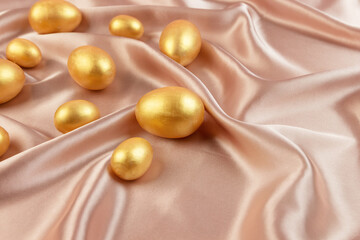 Golden decorative Easter eggs on a background of creamy shiny natural fabric. Soft texture concept. Champagne silk fabric.