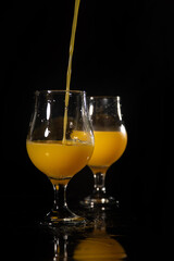 Orange juice, beautiful glasses of orange juice being filled, black background, selective focus.
