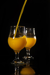 Orange juice, beautiful glasses of orange juice being filled, black background, selective focus.