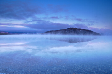 湖面に朝靄の漂う早朝の湖。氷点下の朝の屈斜路湖。阿寒摩周国立公園。北海道、日本。