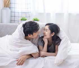 Obraz na płótnie Canvas Happy young Asian couple covered with soft warm white blanket together and smiling together on comfortable bed in bedroom.Valentine couple