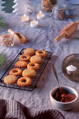 Sandwich cookies filled with hazelnut spread, nougat cream. Christmas Linzer cookies filled on cooling rack, metal plate. Winter decor, linen tablecloth.