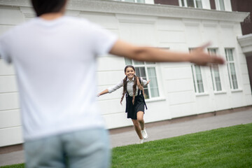 Happy schoolgirl running from school to meeting mom