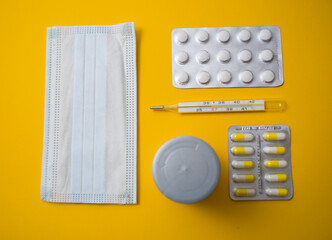 Medical mask, tablets, thermometer on a yellow background. Copy space