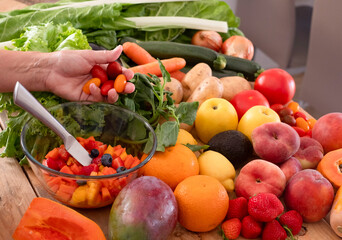The hand of a woman prepare and cut fruits and vegetables. Wooden table with a large group of colorful fruits and vegetables. Healthy eating