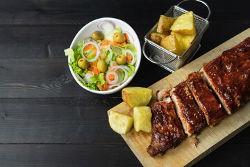 Barbecue ribs and potatoes on a wooden board. Coy space.