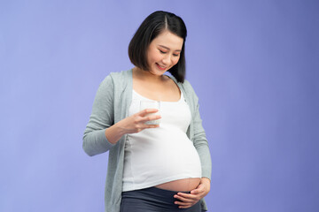 Pregnancy and calcium. Happy pregnant woman holding glass of milk smiling at camera standing over color background