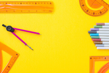 Overhead image of ruler, triangles, protractor, compass and markers on yellow background with copy...