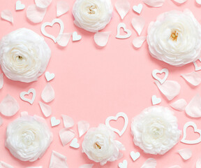 Frame made of cream flowers, petals and hearts on a light pink background