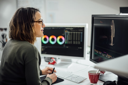Profile view of Female graphic designer at the office with two displays, editing photos and video with a pen tablet. Business woman working concentrated. Freelance worker at Creative office studio.