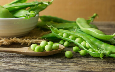Fresh snow pea pods on a wooden spoon set up on the natural wooden table.