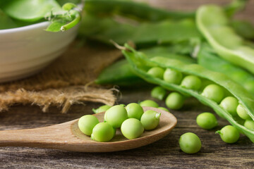 Fresh snow pea pods on a wooden spoon set up on the natural wooden table.
