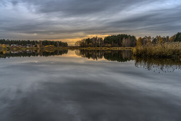 lake in the autumn morning. between sky and water. reflection of gray cloudy sky in calm water. in the distance village houses are visible, autumn colors in nature.