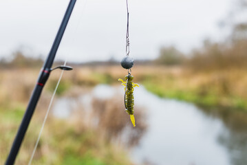 Silicone bait for fishing hanging on a hook on the background of the river. Tackle for fishing. Hobie fishing in nature