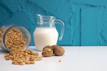 peeled walnuts in a glass jar are scattered on the table, next to there is a jug of milk