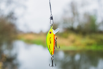 Wobbler yellow and green for fishing on the background of the river. Tackle for fishing. Fishing...