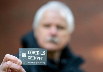 Älterer Herr zeigt Impfnachweis auf einer Chipkarte, die eine COVID-19 Impfung nachweist.
