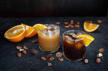 Cold espresso coffee with ice and orange juice in two glass glasses on a dark table with nuts, chocolate and orange. A exhilarant summer drink. 