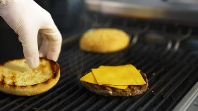 Hands of a person fry buns on grill. Meat cutlet with cheese on top. Fast food concept.