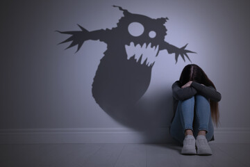 Shadow of monster on wall and scared teenage girl in room © New Africa