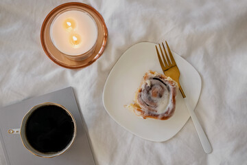 Lifestyle composition with cinnamon bun, coffee and burning candle