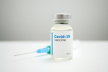Close up of a COVID-19 vaccine bottle and a syringe for injection. A dose of medical treatment for coronavirus disease in a glass bottle on a white clinic table. Medication for virus infection