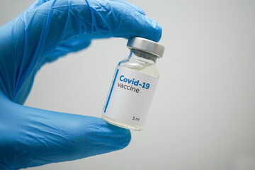 Doctor's hands in blue medical gloves holding a dose of coronavirus vaccine in a glass bottle. Liquid Covid-19 disease treatment for injections. Immunization against corona illness concept.