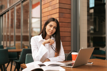 Fototapeta premium Concentrated at work. Young beautiful woman using her laptop while sitting. Beautiful clever cute charming attractive elegant female owner has online meeting indoors