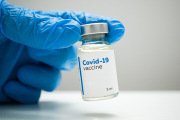 Doctor's hands in blue medical gloves holding a dose of coronavirus vaccine in a glass bottle. Liquid Covid-19 disease treatment for injections. Immunization against corona illness concept.