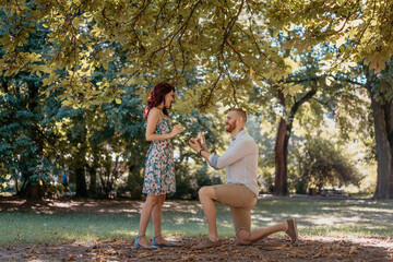 Beautiful young couple in park engagement. Man putting ring on woman hand. Love and emotions...