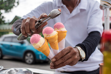 A Sorbetero scoops strawberry and cheese sorbetes into in small wafer cones. Traditional ice cream in the Philippines. - obrazy, fototapety, plakaty