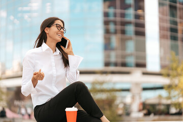 Corporate Communication. Caucasian Businesswoman Talking On Mobile Phone with coffee to go on glass background building