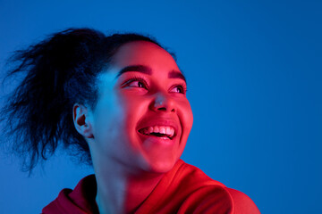 Dreamful. African-american woman's portrait on blue studio background in red-pink neon light....