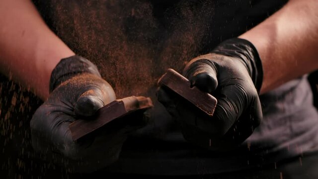 Man hands in black gloves breaking chocolate. Dark chocolate bar breaking in half. Sweet ingredient for cooking dessert. Close up. Slow motion.