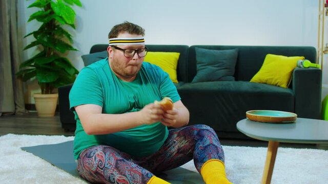 Fat guy have a workout at home in the living room he doing crunches then take a bit of hamburger and continue to do the workout