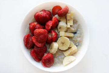 Oatmeal bowl with banana and strawberry, healthy organic food. Summer breakfast. Image with selective focus