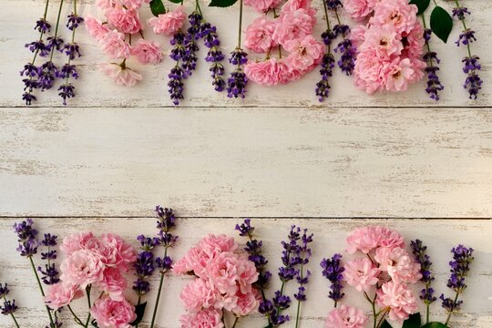Frame with delicate fresh pink roses and lavender flowers on white old wooden background
