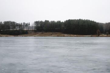 Frozen lake near the forest which is located on a hill