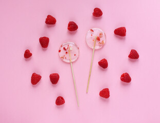 Two transparent lollipops on a pink background. Raspberry berries
