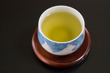 黒い背景の木製のコースターにのった湯呑みに入った緑茶