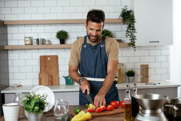 Close up of man cutting vegetables. Attractive man cooking in modern kitchen..