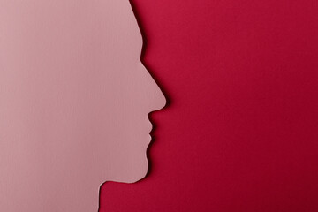 Head silhouette made of paper. Pink paper shaped as a human head with copy space on red paper background.