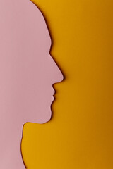 Head silhouette made of paper. Pink paper shaped as a human head with copy space on yellow paper background.