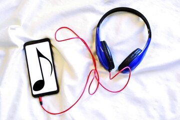 musiс background. Smartphone with note symbol on screen connected to headphones on fabric texture