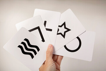 Mano sujetando en abanico las 5 cartas Zener de mentalismo y psicología. Cuadrado, cículo, cruz, olas y estrella © Aida Servi