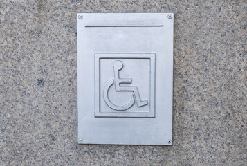 gray granite slab as a background and a plaque, and on it a sign of a disabled person